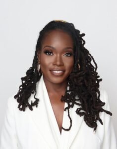 a portrait of a woman smiling with long curly locs wearing a professional white jacket blazer